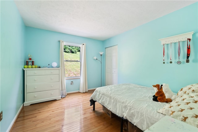 bedroom with light hardwood / wood-style flooring, a textured ceiling, and a closet