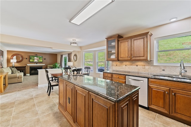 kitchen with an island with sink, backsplash, dark stone counters, sink, and stainless steel dishwasher