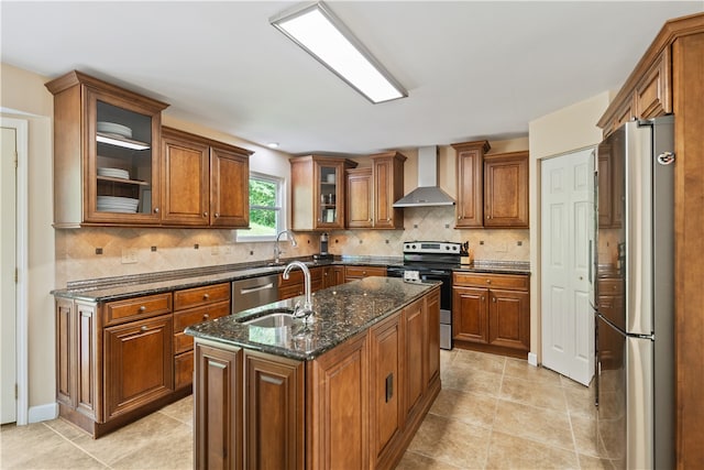 kitchen with wall chimney exhaust hood, stainless steel appliances, dark stone counters, a center island with sink, and sink