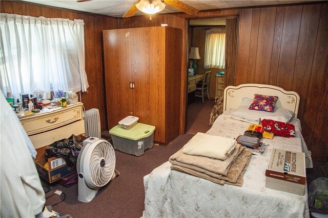 carpeted bedroom with radiator heating unit, wood walls, and ceiling fan