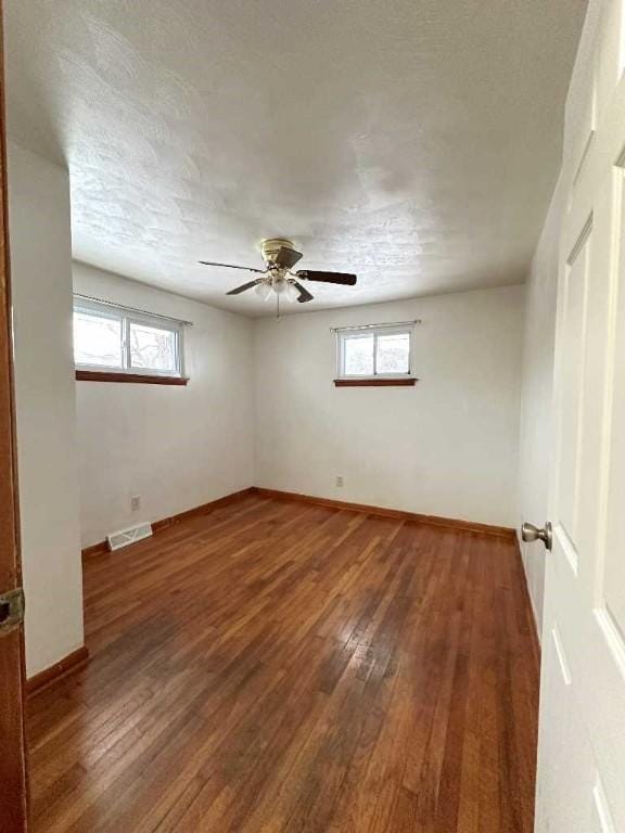 unfurnished room featuring a textured ceiling, dark wood-type flooring, ceiling fan, and plenty of natural light