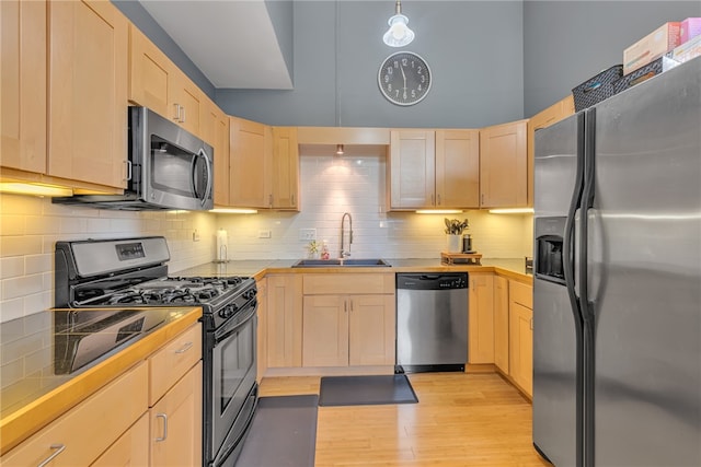 kitchen with stainless steel appliances, sink, backsplash, and light hardwood / wood-style floors