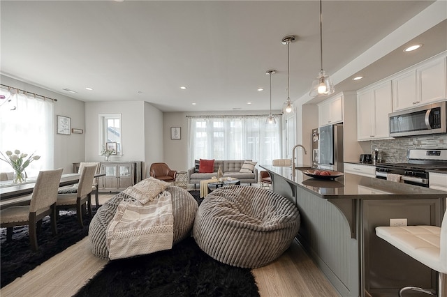 kitchen featuring a kitchen island with sink, light hardwood / wood-style flooring, a kitchen bar, appliances with stainless steel finishes, and white cabinets