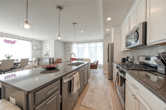 kitchen featuring light wood-type flooring, appliances with stainless steel finishes, white cabinetry, sink, and a center island with sink