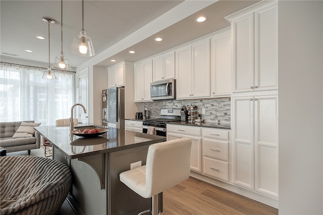 kitchen featuring appliances with stainless steel finishes, light hardwood / wood-style floors, a breakfast bar, hanging light fixtures, and sink