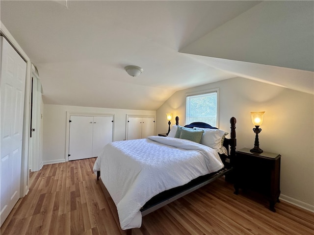 bedroom with two closets, vaulted ceiling, and wood-type flooring