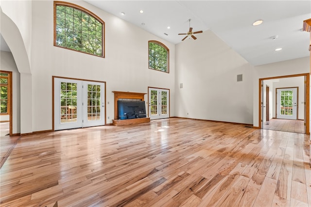 unfurnished living room featuring a high ceiling, french doors, ceiling fan, and light hardwood / wood-style flooring