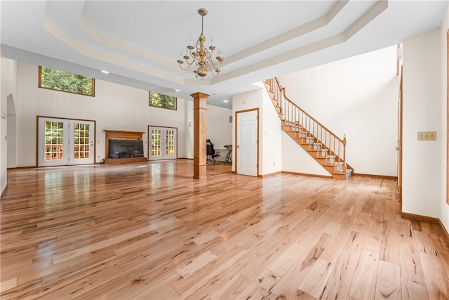 unfurnished living room featuring light hardwood / wood-style flooring, ornate columns, a tray ceiling, and a healthy amount of sunlight