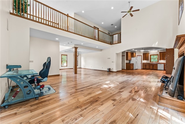 living room with a high ceiling, ceiling fan, light hardwood / wood-style floors, and a healthy amount of sunlight