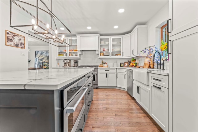 kitchen with white cabinets, stainless steel appliances, light hardwood / wood-style floors, and a notable chandelier