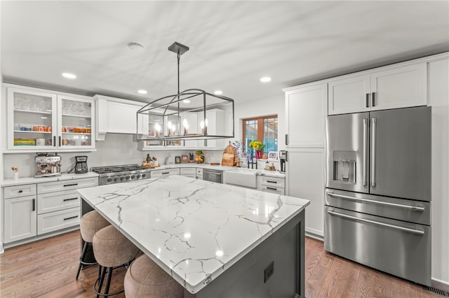 kitchen with white cabinets, hanging light fixtures, light wood-type flooring, stainless steel appliances, and a kitchen island