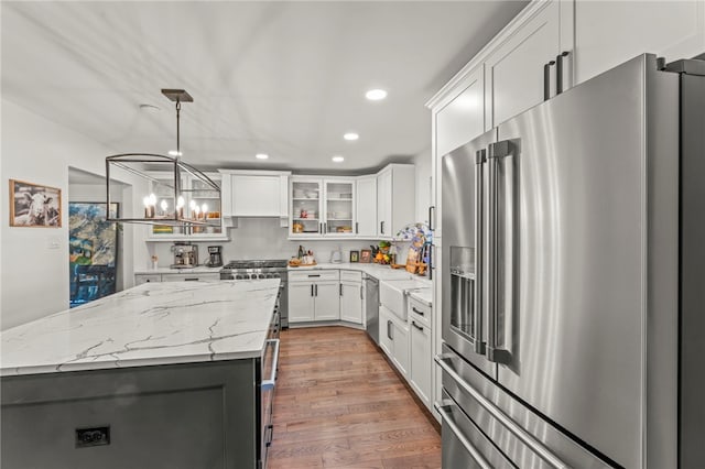 kitchen featuring pendant lighting, high end appliances, light hardwood / wood-style flooring, a center island, and white cabinets