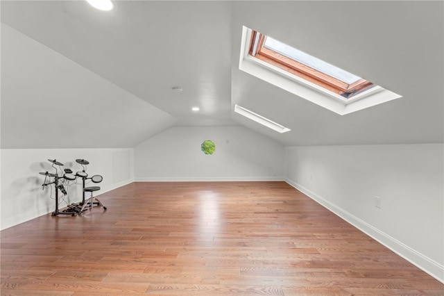 additional living space featuring vaulted ceiling with skylight and light wood-type flooring