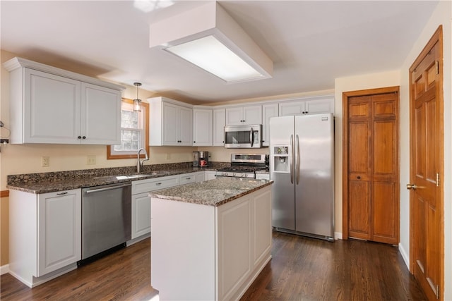 kitchen with decorative light fixtures, appliances with stainless steel finishes, white cabinetry, dark wood-type flooring, and a kitchen island