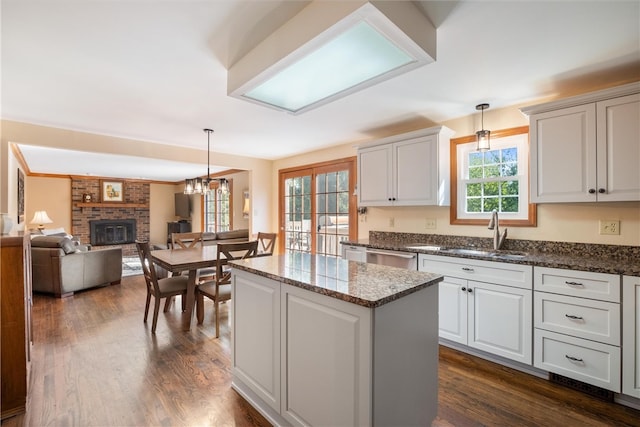 kitchen with pendant lighting, white cabinetry, a brick fireplace, and sink