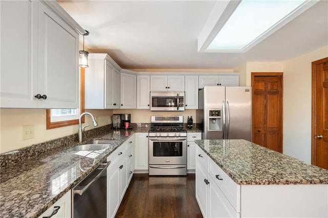 kitchen with appliances with stainless steel finishes, dark hardwood / wood-style flooring, sink, dark stone counters, and pendant lighting