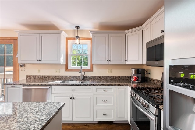 kitchen with white cabinets, stone counters, appliances with stainless steel finishes, sink, and pendant lighting