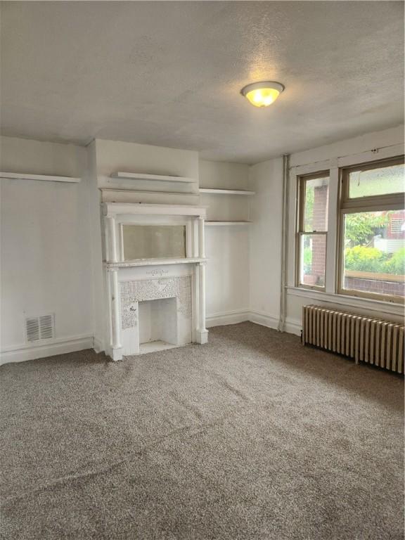 2622 Milburn St, Mckeesport, PA 15132 - unfurnished living room with radiator heating unit, carpet floors, visible vents, and a textured ceiling