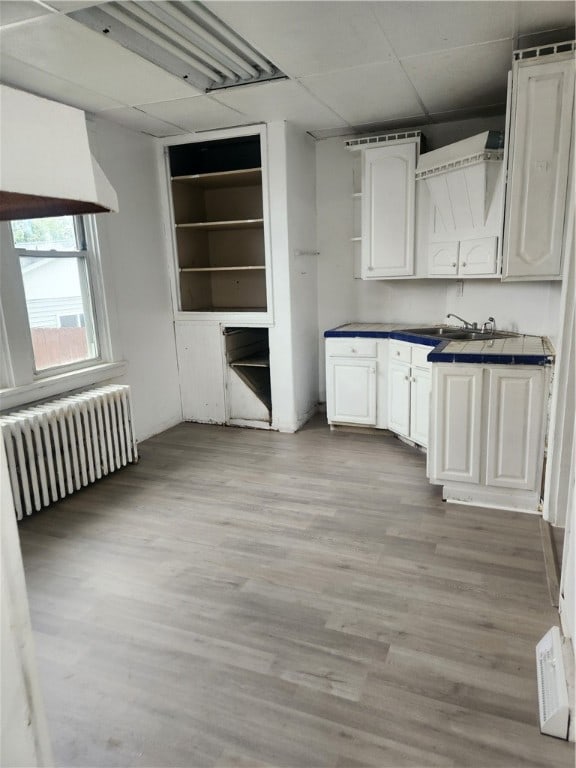 kitchen featuring radiator, a paneled ceiling, light hardwood / wood-style floors, and white cabinetry