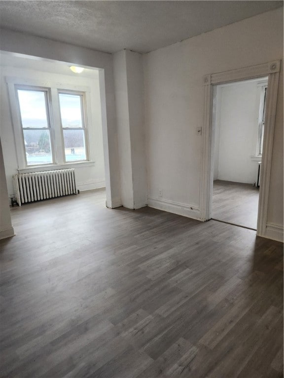 unfurnished room with radiator, a textured ceiling, and dark wood-type flooring