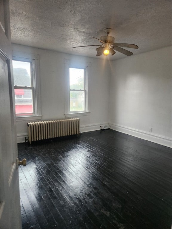 empty room with ceiling fan, a textured ceiling, dark wood-type flooring, and radiator heating unit