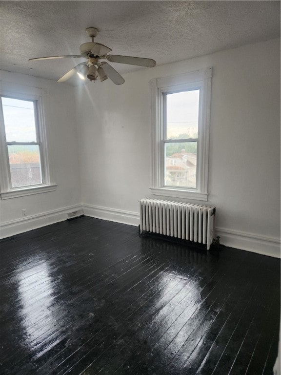 unfurnished room featuring plenty of natural light, radiator heating unit, dark hardwood / wood-style floors, and a textured ceiling