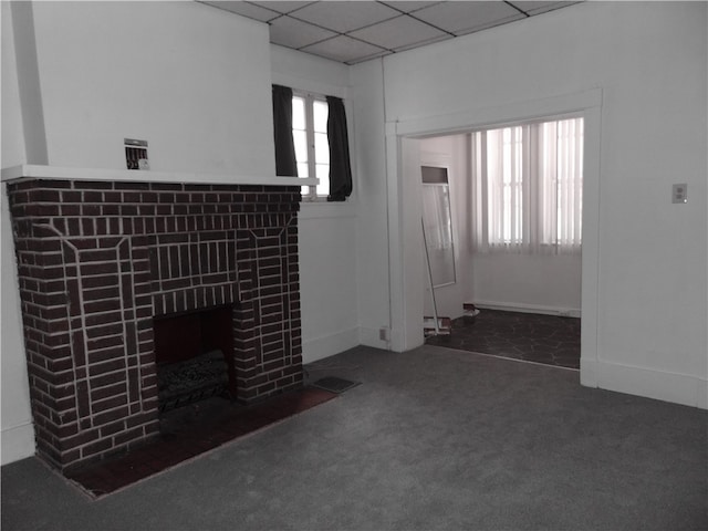 unfurnished living room featuring a wealth of natural light, a brick fireplace, dark carpet, and a drop ceiling