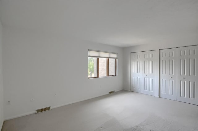 unfurnished bedroom with two closets and light colored carpet