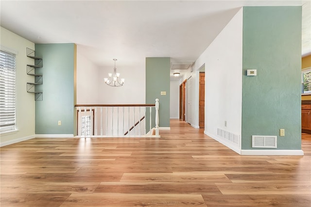 empty room featuring a wealth of natural light, hardwood / wood-style floors, and a notable chandelier