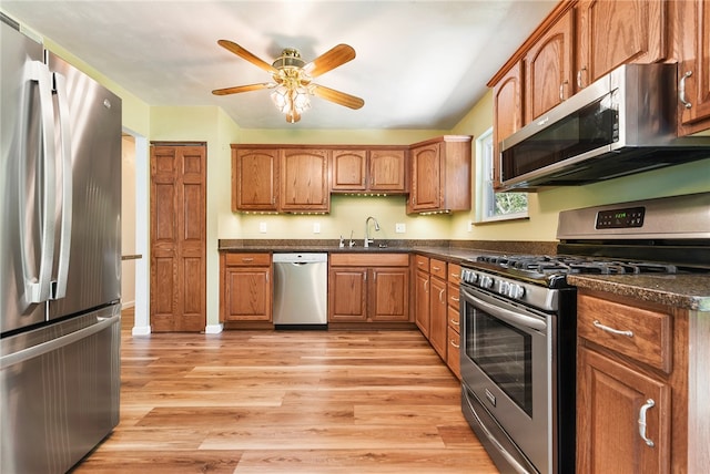 kitchen featuring ceiling fan, sink, dark stone counters, appliances with stainless steel finishes, and light wood-type flooring