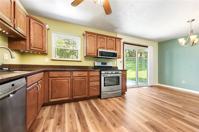 kitchen featuring appliances with stainless steel finishes, light wood-type flooring, ceiling fan with notable chandelier, sink, and pendant lighting