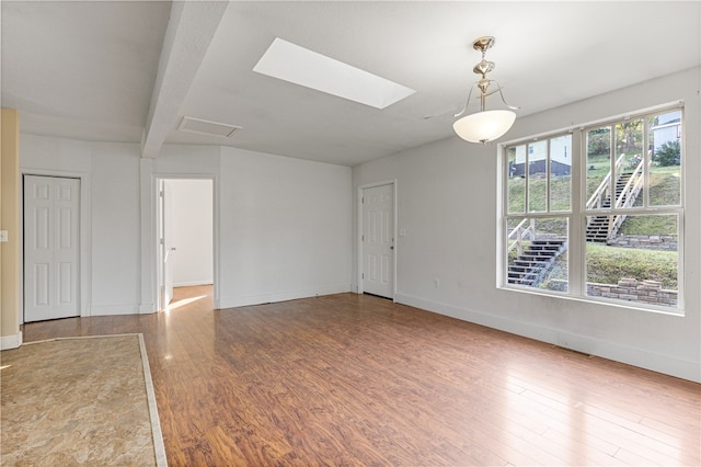 unfurnished room featuring beamed ceiling, wood-type flooring, and a skylight