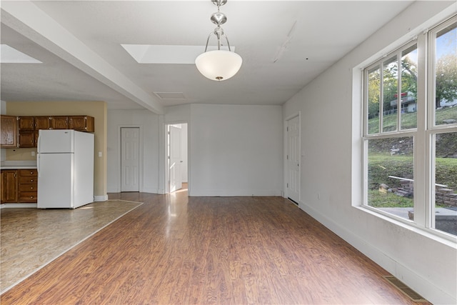 unfurnished living room with plenty of natural light, hardwood / wood-style floors, beam ceiling, and a skylight