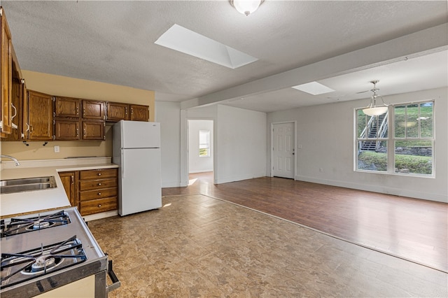 kitchen featuring a skylight, light hardwood / wood-style flooring, decorative light fixtures, white refrigerator, and sink