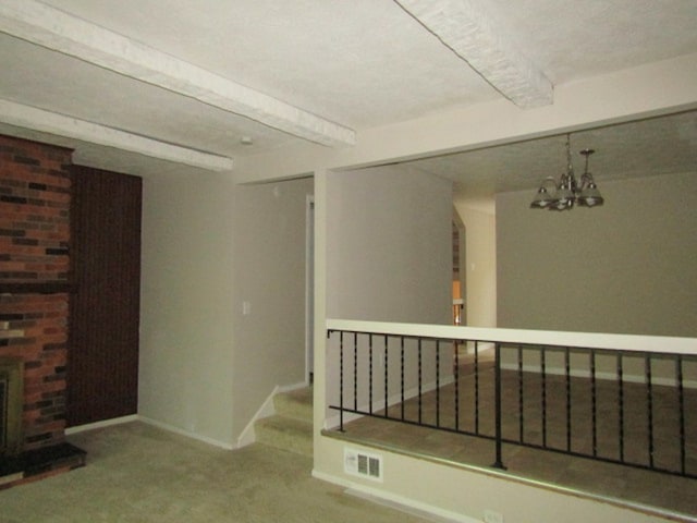 unfurnished room with carpet flooring, an inviting chandelier, beamed ceiling, and a brick fireplace