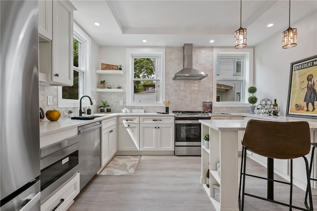 kitchen with a notable chandelier, stainless steel appliances, sink, wall chimney range hood, and white cabinets