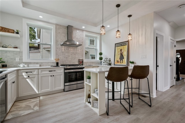 kitchen with tasteful backsplash, light hardwood / wood-style flooring, a kitchen breakfast bar, appliances with stainless steel finishes, and wall chimney range hood