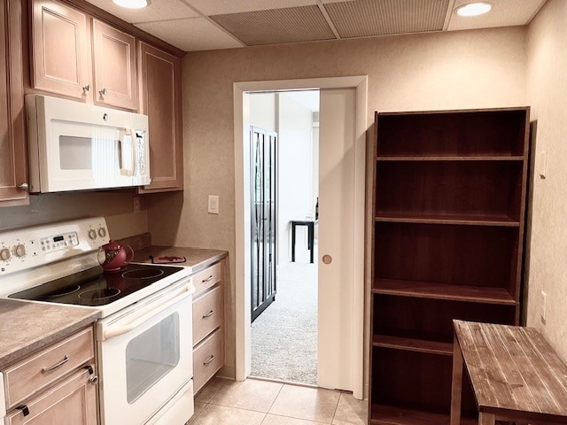 kitchen with light tile patterned floors, white appliances, and a drop ceiling