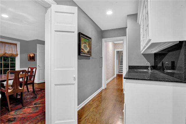 kitchen featuring white cabinets, dark stone countertops, hardwood / wood-style floors, sink, and ornamental molding