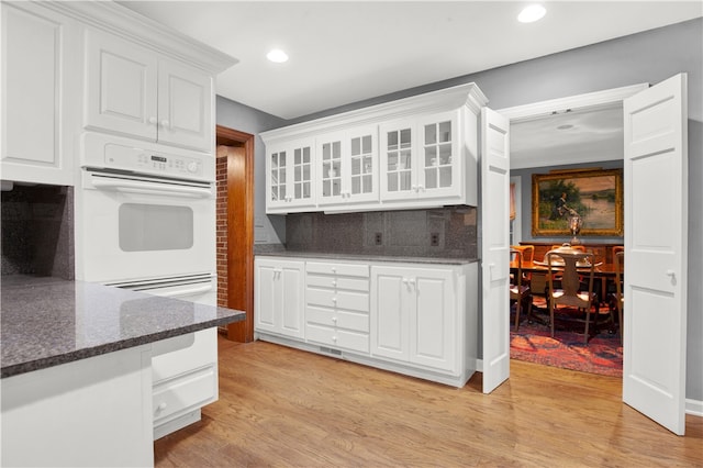 kitchen with tasteful backsplash, dark stone counters, white cabinetry, and light hardwood / wood-style flooring