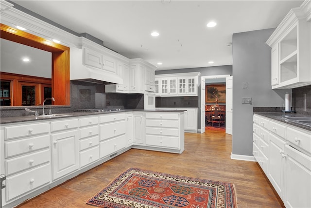 kitchen with oven, backsplash, sink, white cabinetry, and light wood-type flooring