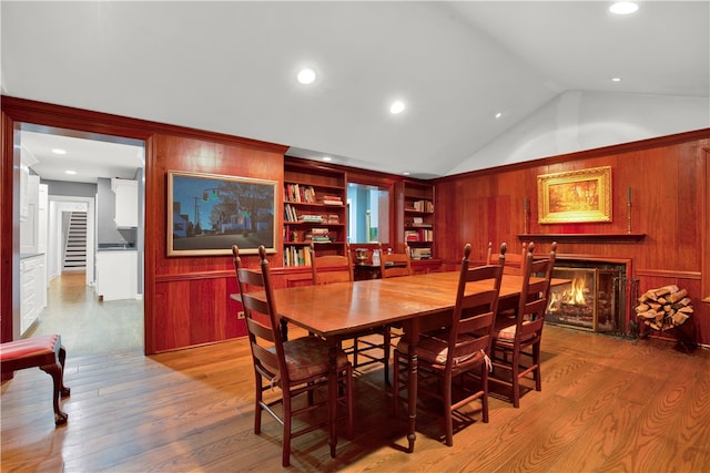 dining area with built in shelves, lofted ceiling, wooden walls, and light hardwood / wood-style floors