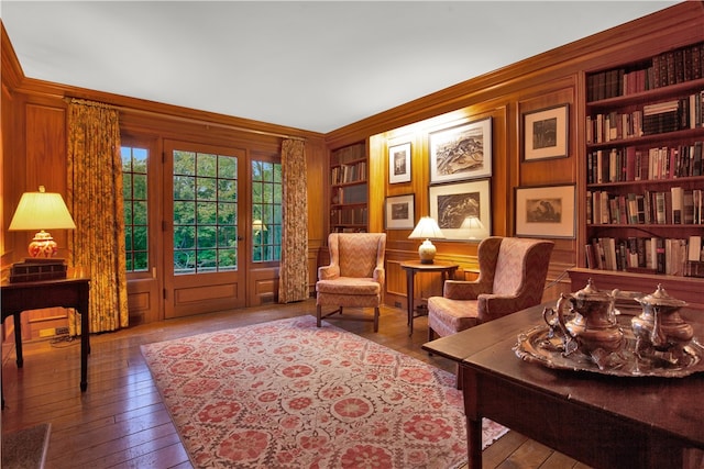 living area with built in shelves, hardwood / wood-style flooring, wooden walls, and crown molding