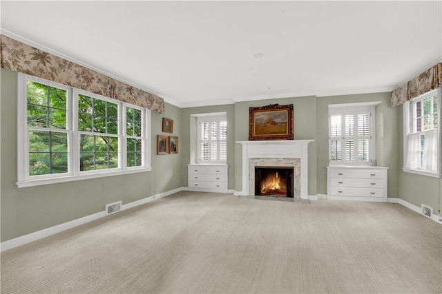 unfurnished living room featuring a high end fireplace, crown molding, a healthy amount of sunlight, and carpet floors