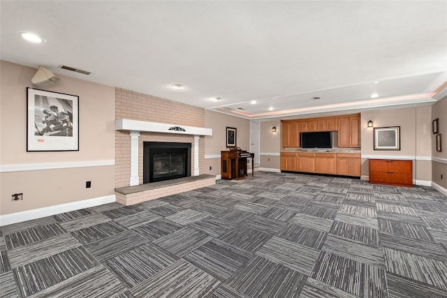 unfurnished living room featuring dark carpet, a fireplace, a raised ceiling, and crown molding