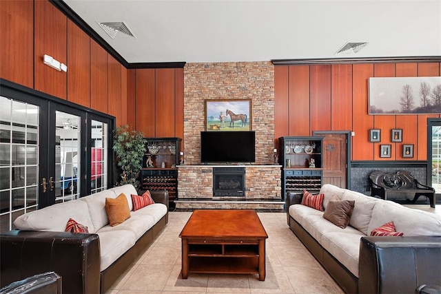 tiled living room featuring french doors, wooden walls, and a stone fireplace