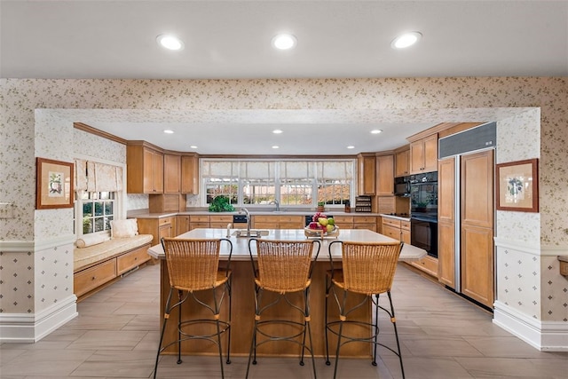 kitchen with black double oven, sink, a center island with sink, and a kitchen breakfast bar