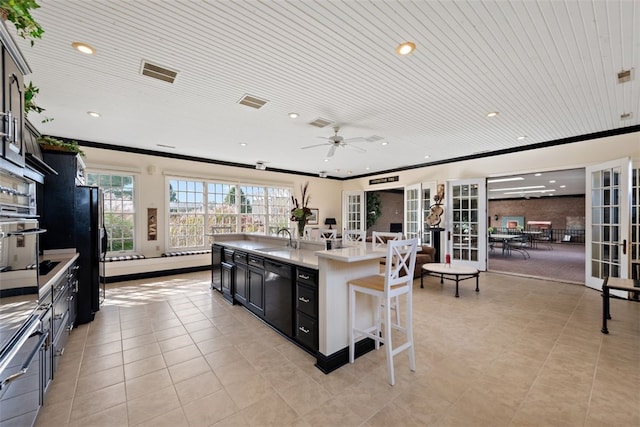 kitchen with crown molding, sink, black appliances, an island with sink, and ceiling fan