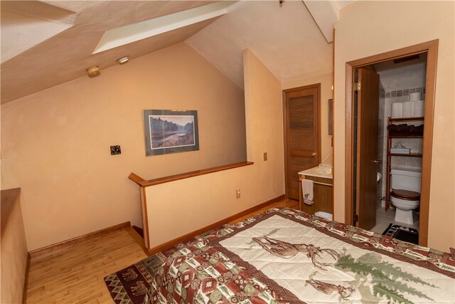 bedroom featuring ensuite bath, light hardwood / wood-style flooring, and lofted ceiling