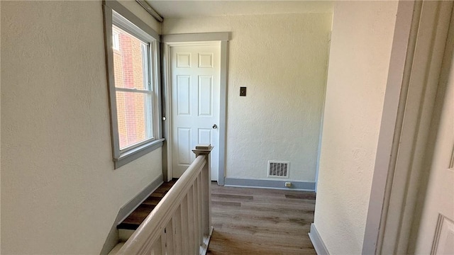 hall with plenty of natural light, an upstairs landing, visible vents, and a textured wall